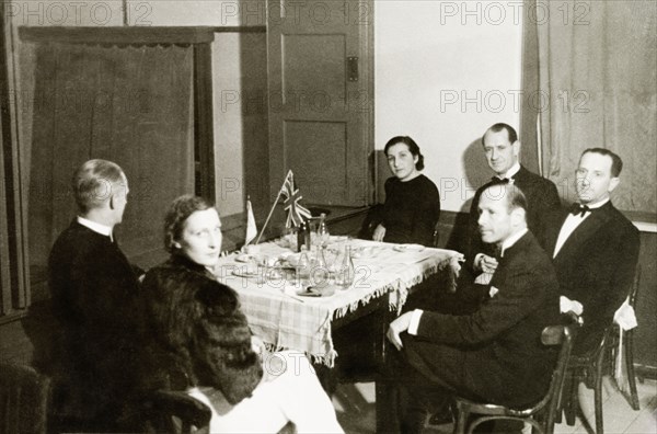 An informal supper, Jersualem. William Ryder McGeagh (centre, back row), District Commissioner in Jerusalem, and his wife (second from left) relax with a group of smartly dressed friends after an informal supper. The table in front of them is decorated with a Jewish flag and a union jack. An original caption identifies the others as 'Shadforth', 'Goldman' and 'Mr and Mrs Kisselov'. Jerusalem, British Mandate of Palestine (Israel), circa 1939. Jerusalem, Jerusalem, Israel, Middle East, Asia.