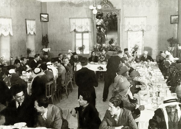 Arab officials attend a formal meal . A number of Palestinian Arab officials sit around long dining tables at a formal dinner reception. Several wear traditional Arab 'keffiyehs' (headdresses), whilst others are dressed in military uniforms with spiked helmets, possibly officers of the Transjordan Arab Legion. British Mandate of Palestine (Israel), circa 1939. Israel, Middle East, Asia.