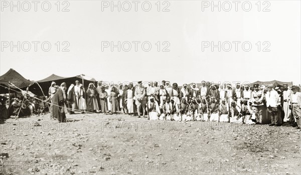 A meeting with Arab leaders. Two British officials pose for a group portrait with Arab leaders during a meeting at a desert camp. A line of armed Arab men kneel in the front row. British Mandate of Palestine (Israel), circa 1940. Israel, Middle East, Asia.