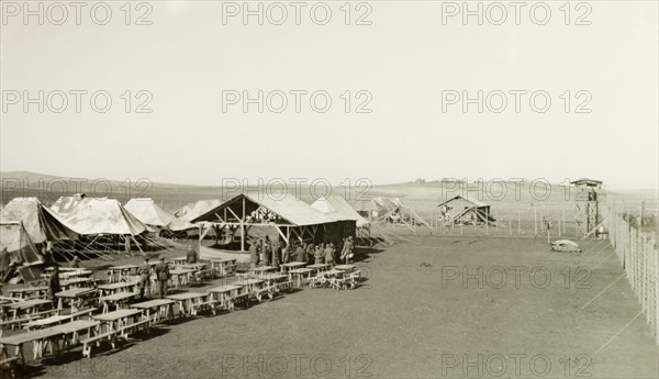 Mess tent at a British Army camp. Rows of tables are lined up outside the mess tent of a British Army camp, which is protected by a high, barbed wire fence. British Mandate of Palestine (Israel), circa 1940. Israel, Middle East, Asia.