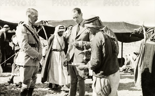 Coffee break at a council in the desert. William Ryder McGeagh (centre), District Commissioner in Jerusalem, and a British official in military uniform are served coffee during a council with Arab leaders at a camp in the desert. British Mandate of Palestine (Israel), circa 1940. Israel, Middle East, Asia.
