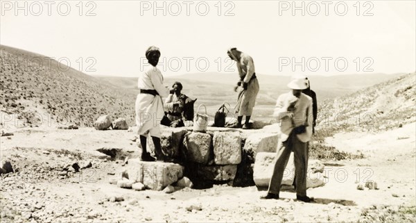 Drawing water from a desert well. A party of travellers draws water from a desert well in Al-Masfara, a mountainous region to the west of the Dead Sea. An original caption identifies one of the men as Dr. Krikorian, possibly Samuel Krikorian, an Armenian missionary of the Church of the Nazarene. British Mandate of Palestine (West Bank, Middle East), 2-9 April 1941., West Bank, West Bank (Palestine), Middle East, Asia.