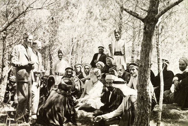 British officials meet Arab mukhtars . British officials talk to Arab mukhtars (headmen) in a woodland clearing at a party organised by the District Commissioner. Edward Keith-Roach, District Governor of Jerusalem, stands (second from left) whilst his wife sits at the centre of the group. Qubeiba, British Mandate of Palestine (West Bank, Middle East), 1941. Qubeiba, West Bank, West Bank (Palestine), Middle East, Asia.