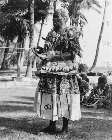 Fijian man with a 'tabua'. A Fijian man wearing face paint and ceremonial costume made from 'masi' (bark cloth) holds a 'tabua' (polished whale's tooth) in one hand. The tabua is an important cultural item in Fijian society, which was traditionally given as a gift of atonement or esteem. Fiji, 1965. Fiji, Pacific Ocean, Oceania.