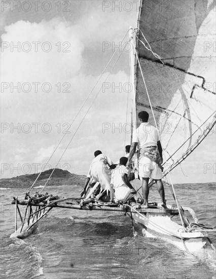 A 'drua' off the coast of Fiji. Four men crew a 'drua' (Fijian catamaran) off the coast of Fiji. Fiji, 1965. Fiji, Pacific Ocean, Oceania.
