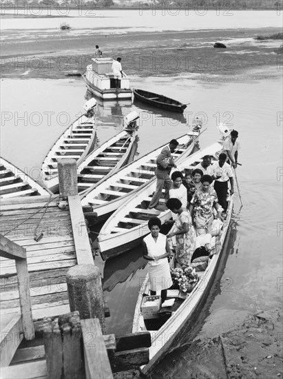 At a wooden jetty on the Nasilai River. A motorised canoe full of people carrying goods to market prepares to depart from a wooden jetty on the Nasilai River. Viti Levu, Fiji, 1965., Viti Levu, Fiji, Pacific Ocean, Oceania.