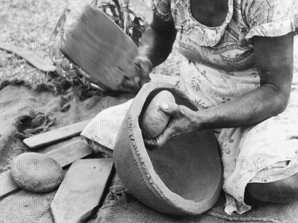 Making a clay pot, Fiji. A kneeling woman shapes a clay pot using a rounded stone and a wooden paddle. Fiji, 1965., Fiji, Pacific Ocean, Oceania.