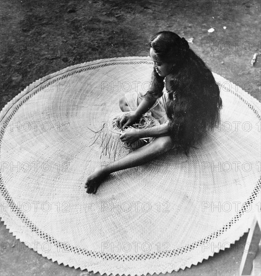 Weaving a mat from pandunas leaves . A Tahitian woman concentrates as she puts the finishing touches to a circular mat made from woven pandunas leaves. Tahiti, French Polynesia, 1965., Windward Islands (including Tahiti), French Polynesia, Pacific Ocean, Oceania.