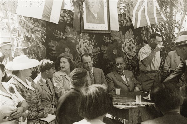 Opening of the Benes Garden in Gan Yavne. William Ryder McGeagh (centre), District Commissioner in Jerusalem, attends the opening of the Benes Garden in commemoration of deposed Czech President, Edvard Benes. Above him hangs a framed portrait of Benes, surrounded by a Jewish flag and a union jack. Gan Yavne, British Mandate of Palestine (Central Israel), 4 June 1944., Central (Israel), Israel, Middle East, Asia.