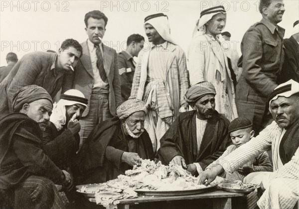 Arab meal at a military recruitment meeting. A group of Arab men wearing turbans and 'keffiyehs' (headdresses) eat a meal with their hands at a military recruitment meeting conducted by British colonial and military officers. Al Faluja, British Mandate of Palestine (South Israel), 1944., South (Israel), Israel, Middle East, Asia.