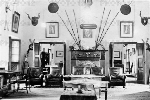 Drawing room at the Police Training School. Interior shot of the Mess inside the Police Training School at Moradabad. Hung on the wall, above a grand fireplace and five leather armchairs, are several framed portraits and numerous spears, shields and hunting trophies. Moradabad, United Provinces (Uttar Pradesh), India, circa 1933. Moradabad, Uttar Pradesh, India, Southern Asia, Asia.