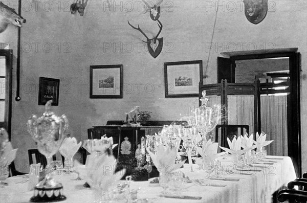 Dining room at the Police Training School. Various trophies form the centrepiece of a table that has been set for a formal dinner for the Inspector-General of Police, Harold Poe, at Moradabad's Police Training School. The wall behind is decorated with framed pictures and hunting trophies. Moradabad, United Provinces (Uttar Pradesh), India, circa 1933. Moradabad, Uttar Pradesh, India, Southern Asia, Asia.