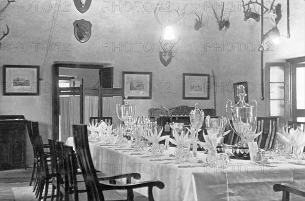 Dining room at the Police Training School. Various trophies form the centrepiece of a table that has been set for a formal dinner for the Inspector-General of Police, Harold Poe, at Moradabad's Police Training School. The wall behind is decorated with framed pictures and hunting trophies. Moradabad, United Provinces (Uttar Pradesh), India, circa 1933. Moradabad, Uttar Pradesh, India, Southern Asia, Asia.