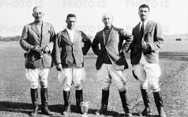 Winning polo players at Bareilly. Portrait of four male polo players after winning the Bareilly Polo Cup, all dressed in dark jackets, white breeches and high leather boots. A large trophy stands at their feet and two of the group hold smaller trophies of their own. The man on the far left is identified as Hugh Inglis of the Indian Police, who was also Principal of the Police Training School at Moradabad. On the right is W M WrightBareilly, United Provinces (Uttar Pradesh), India, February 1934. Bareilly, Uttar Pradesh, India, Southern Asia, Asia.