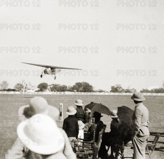 Flight over Moradabad'. A handful of spectators shield themselves from the sun with umbrellas as they watch a Spider aircraft coming into land at the Indian Pageant at Moradabad. A barrier in the distance bears the slogan: "Barnard Uses Castrol". Moradabad, United Provinces (Uttar Pradesh), India, February 1934. Moradabad, Uttar Pradesh, India, Southern Asia, Asia.