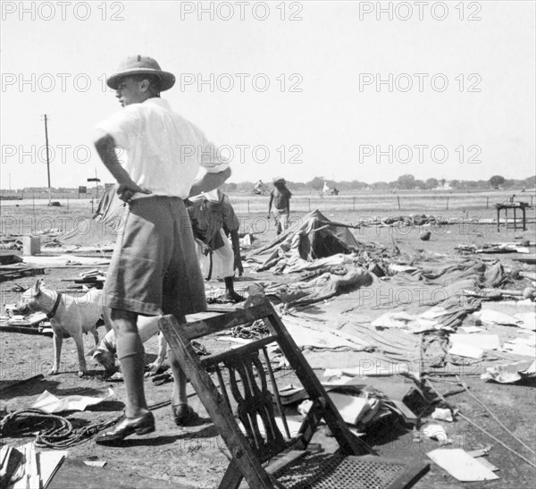 Storm damage at an Indian Police camp. George Boon stands with his hands on his hips as he surveys storm damage with his dog, Sally, at the camp of James Ferguson, Indian Police. United Provinces (Uttar Pradesh), India, 1936., Uttar Pradesh, India, Southern Asia, Asia.