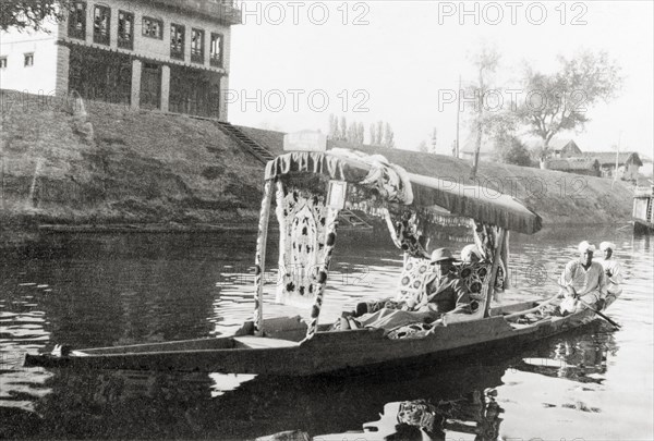 Water taxi on a Srinagar canal. Majid Ullah in the shikari 'Blue Heaven' as he is ferried along a canal in a water taxi. Srinagar, Jammu and Kashmir, India, May 1934. Srinagar, Jammu and Kashmir, India, Southern Asia, Asia.