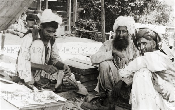 A visit to the cobbler. Two elderly men visit a cobbler who squats on the ground, mending boots in an outdoor workshop. Uri, Jammu and Kashmir, India, 1934. Srinagar, Jammu and Kashmir, India, Southern Asia, Asia.
