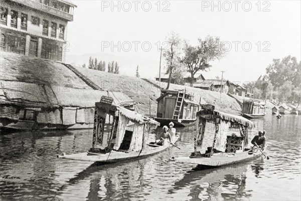 Water taxis on a Srinagar canal. Two water taxis travel along Lake Dal past a several moored shikaras (houseboats). Srinagar, Jammu and Kashmir, India, 1934. Srinagar, Jammu and Kashmir, India, Southern Asia, Asia.