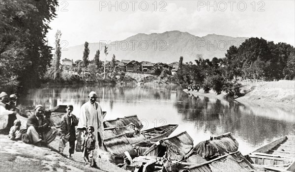 Evening on the Jhelum'. A group of men and small children mill about on a steep riverbank above the Jhelum River, where a row of covered boats is moored. Srinagar, Jammu and Kashmir, India, 1934., Jammu and Kashmir, India, Southern Asia, Asia.