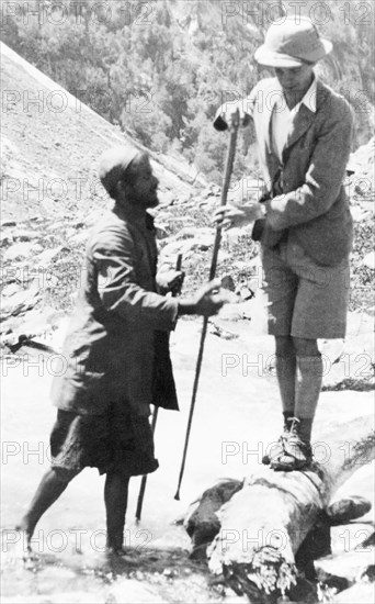 Preparing to cross a Kashmiri stream. George Boon balances precariously on a log as he prepares to cross a fast-flowing mountain stream near Sekwas Pass. Jammu and Kashmir, India, June 1934., Jammu and Kashmir, India, Southern Asia, Asia.