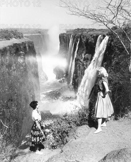 Publicity shot of Victoria Falls, 1961. A government publicity shot of two European woman standing on the edge of a cliff overlooking Victoria Falls, a spectacle known locally as 'Mosi-oa-Tunya' or the 'smoke that thunders'. Matabeleland, Southern Rhodesia (Matabeleland North, Zimbabwe), October 1961., Matabeleland North, Zimbabwe, Southern Africa, Africa.