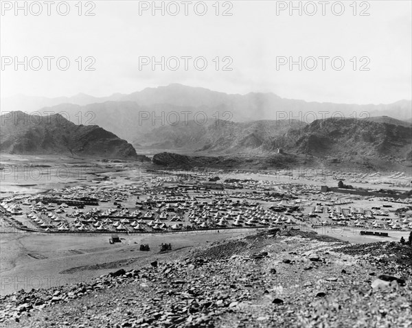 Military camp at Landi Kotal. View looking south across an Indian Army camp, located in a mountain valley near the Khyber Pass. Protected by earthworks, the camp contains rows of bell tents and military vehicles, with a large, walled fortification to the right. An inscription on a distant mountainside reads: '54th M.Corps'. Landi Kotal, North West Frontier Province, India (Federally Administered Tribal Areas, Pakistan), circa 1919. Landi Kotal, Federally Administered Tribal Areas, Pakistan, Southern Asia, Asia.