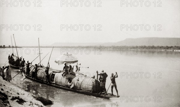 The Sarkin of Muye in his state canoe. The Sarkin (King) of Muye sits beneath a ceremonial umbrella with two trumpet players as he is ferried along the River Niger in his state canoe. Muye, Northern Territories (Niger State), Nigeria, February 1947. Muye, Niger, Nigeria, Western Africa, Africa.