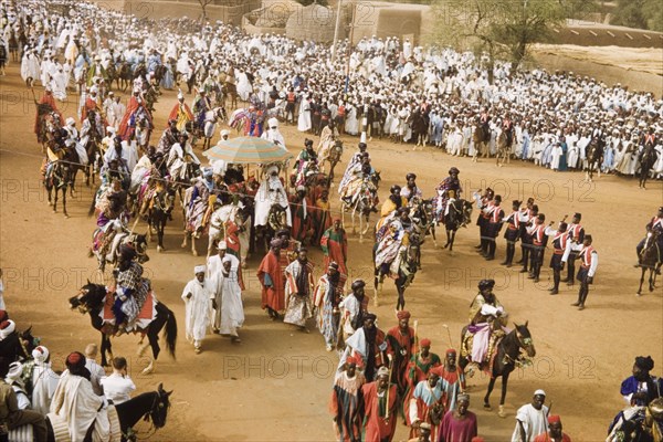 The Emir of Kano rides into the Residency. The new Emir of Kano, Alhaji Ado Bayero, rides into the Residency beneath a ceremonial umbrella during a colourful procession for Sallah, an Islamic celebration held to mark the end of Ramadan. Kano, Nigeria, 1963. Kano, Kano, Nigeria, Western Africa, Africa.