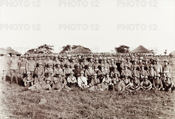 First Service Battalion of the Nigerian Regiment. Group portrait of British officers from the First Service Battalion of the Nigerian Regiment. African soldiers of the Royal West African Frontier Force can be been assembled in rows in the background. Zaria, Nigeria, November 1918. Zaria, Kaduna, Nigeria, Western Africa, Africa.