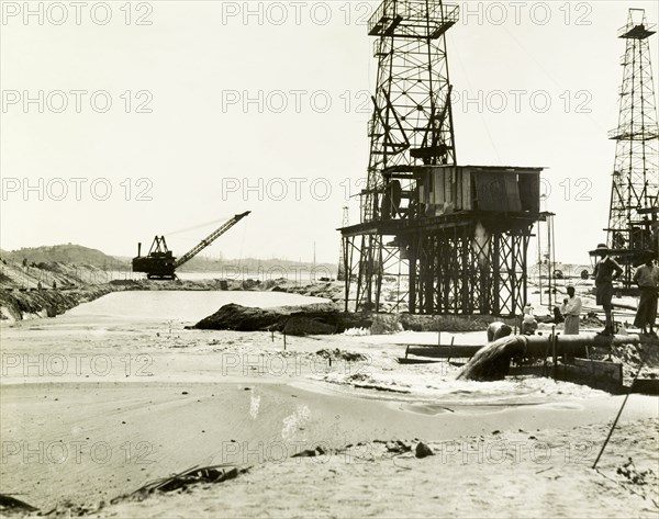 Raising the land at the Chauk-Lanywa oilfield. Construction workers use a dredger to pump sand onto the Chauk-Lanywa oilfield, raising the land level to protect against the annual floods of the Ayeyarwady River. Related images show a raised road with a steep embankment stretching out into the river, built to provide dry-land access to the oilfield and its network of oil derricks. Chauk, Burma (Myanmar), circa 1931. Chauk, Magway, Burma (Myanmar), South East Asia, Asia.