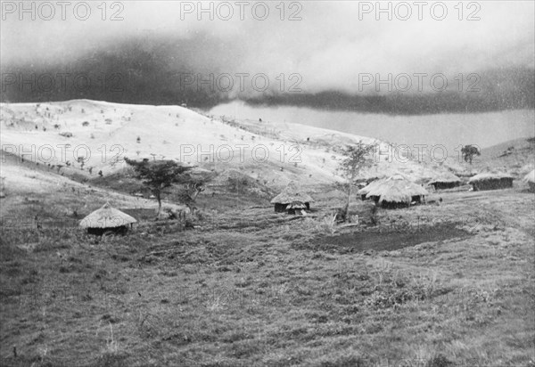 Storm clouds over Lumbwa. Storm clouds gather over a small valley settlement in the hills. Near Lumbwa, Rift Valley, Kenya, circa 1934. Lumbwa, Rift Valley, Kenya, Eastern Africa, Africa.