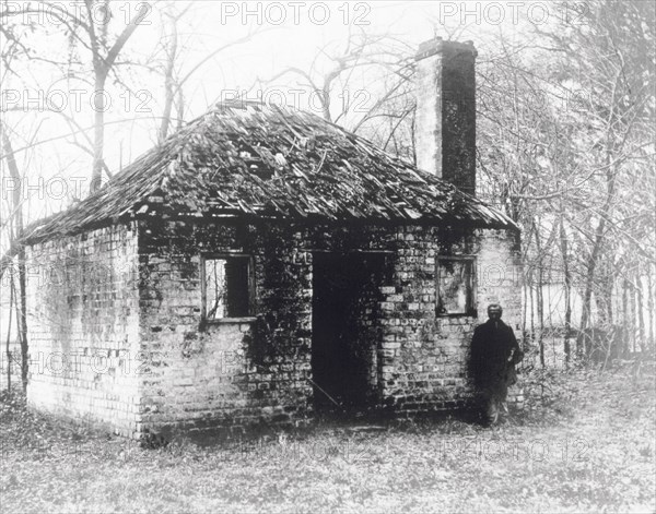 Former slave accommodation. A man stands outside a dilapidated building that was once used to accommodate plantation slaves. Savannah, Georgia, United States of America, circa 1900. Savannah, Georgia, United States of America, North America, North America .