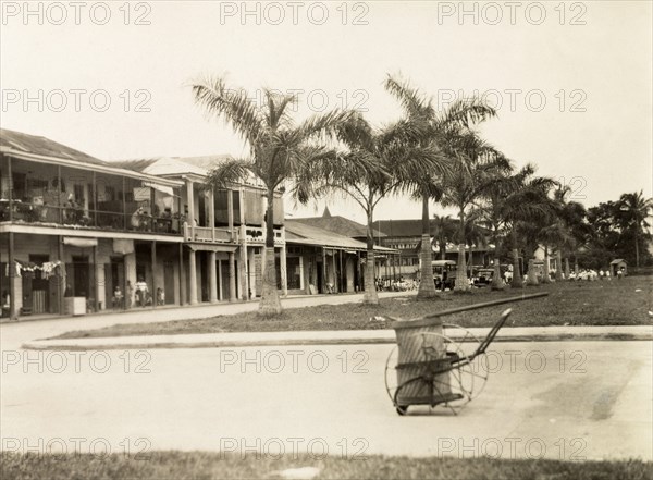 A residential street in Colon. A patch of grass flanked by palm trees leads up to a residential street in Colon, an area that is identifed in an original caption as the 'poor quarter'. Colon, Panama, circa 1930. Colon, Colon, Panama, Central America, North America .