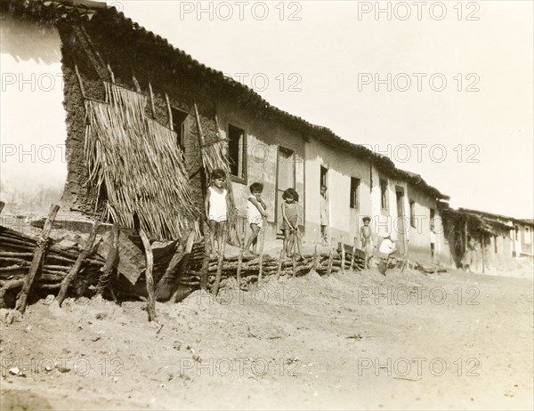 A row of houses in Natal, Brazil. Brazilian children stand outside a row of single-storey houses with corrugated iron roofs. The outer wall of the nearest house has not yet been plastered, revealing its mud brick construction below. Natal, Brazil, circa 1931. Natal, Brazil, Brazil, South America, South America .