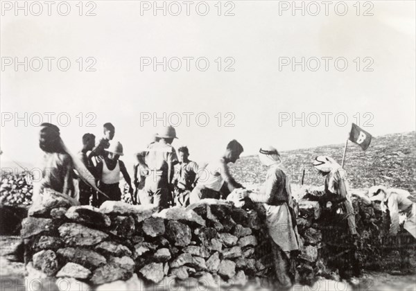 Building a camp at Kafr Ra'i. A group of Arab men construct a stone wall under British military supervision during the Great Uprising (1936-39). An original caption comments that they are building "camp", perhaps a military base or refugee camp. Kafr Ra'i, British Mandate of Palestine (West Bank, Middle East), circa 1938., West Bank, West Bank (Palestine), Middle East, Asia.