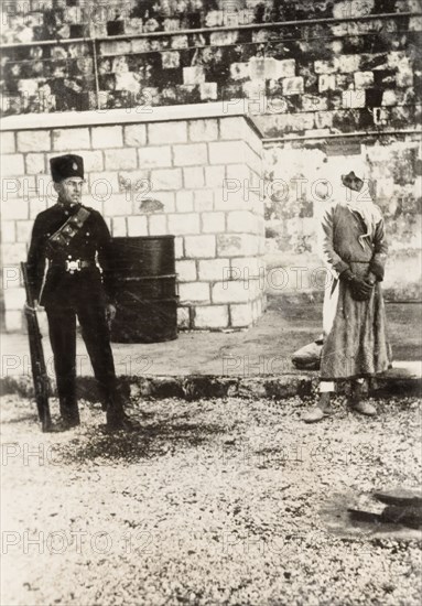 Arab prisoner of the Great Uprising. A young Arab prisoner stands handcuffed in a courtyard, under police supervision, after having been sentenced to death for committing rebel acts during the Great Uprising (1936-39). British Mandate of Palestine (Middle East), circa 1938., Middle East, Asia.