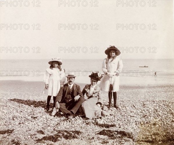The Murray family on the beach. James and Minnie Murray sit on a shingle beach as they pose for a portrait with their two daughters, Jessie and Enid, during an excursion to the seaside. Probably Eastbourne, England, circa 1907. Eastbourne, Sussex, England (United Kingdom), Western Europe, Europe .