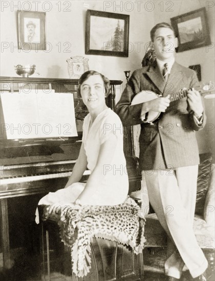 A musical family, Eastbourne. James Murray plays a banjo whilst his sister sits at the piano in the drawing room of an English house. This portrait was taken shortly before James travelled to India to take over the family chronometry business in Calcutta (Kolkata). Eastbourne, England, 1929. Eastbourne, Sussex, England (United Kingdom), Western Europe, Europe .