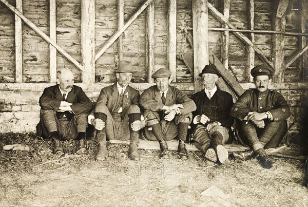 Smoking break at Hardwick Estate. Five men from a shooting party sit against a wall, smoking, during a hunt at Hardwick Estate. Derbyshire, England, circa 1918., Derbyshire, England (United Kingdom), Western Europe, Europe .