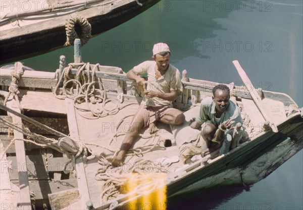 Traders in Aden harbour. Two traders relax in the sun on the deck of a dhow in Aden harbour. April 1964. Mombasa, Coast, Kenya, Eastern Africa, Africa.