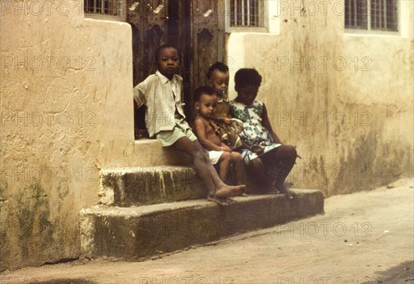 Children in Mombasa. Four children sit on stone steps outside a doorway in Mombasa. Mombasa, Kenya, April 1964. Mombasa, Coast, Kenya, Eastern Africa, Africa.