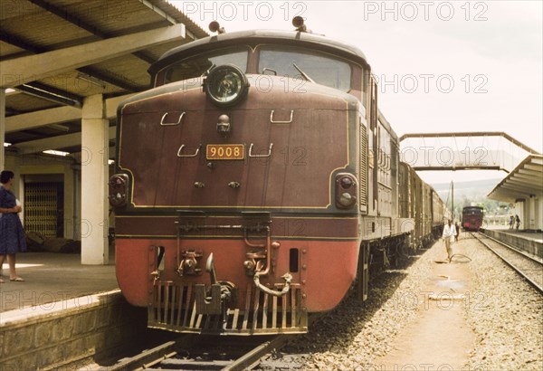 The train pauses for an hour'. A Uganda Railways locomotive waits in a station, pausing for a rest stop on its journey from Kampala to Mombasa. West Kenya, April 1964., West (Kenya), Kenya, Eastern Africa, Africa.