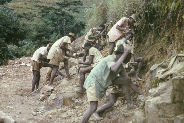 Road building at Mafuga Forest. A group of labourers drill rocks with hand chisels in Ishasha Valley, creating shot holes to be filled with gelignite for blasting. These porters were employed by a forestry team who were clearing a track in Mafuga Forest nursery. Kigezi, South West Uganda, September 1963., West (Uganda), Uganda, Eastern Africa, Africa.