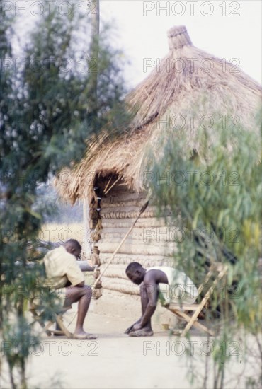 Park Rangers play omweso. Two off-duty Park Rangers play omweso ('mweso'), an ancient mancala game, in the dust at Ishasha River Camp in the Queen Elizabeth National Park. A related caption comments: "(The game) is normally played on a portable wooden board with wild banana seeds as 'men'". West Uganda, July 1962., West (Uganda), Uganda, Eastern Africa, Africa.