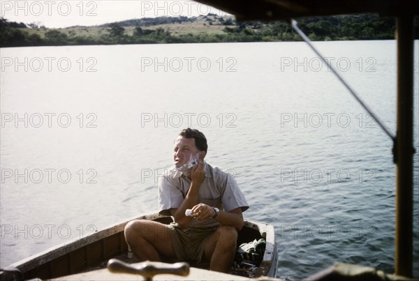 Shaving on Lake Victoria. District Forest Officer Bob Plumptre sits shaving in the stern of a dinghy during a survey safari to Buvuma Island on Lake Victoria. Uganda, 1962., Central (Uganda), Uganda, Eastern Africa, Africa.