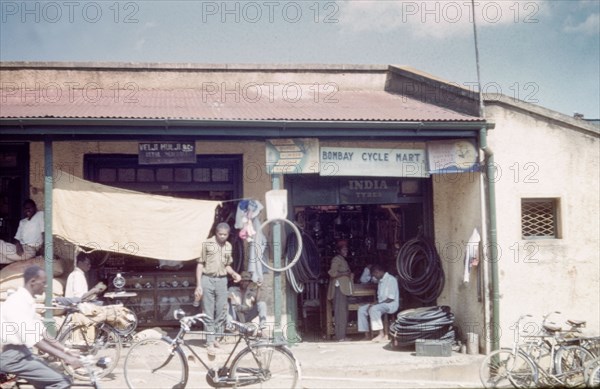Dukas in Kampala bazaar. A duka (shop) selling clocks and a bicycle repairer in Kampala Road. Kampala, Uganda, 1960. Kampala, Central (Uganda), Uganda, Eastern Africa, Africa.