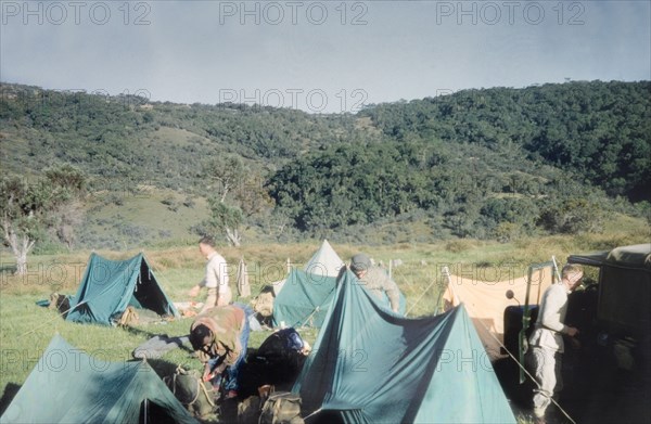 Camp at Mount Elgon roadhead'. Members of the Uganda Mountain Club set up camp on an expedition to Mount Elgon on the Kenya-Uganda border. A related caption comments: "The African in the foreground is Tim Bazarrabusa: an altogether remarkable man who, in spite of coming from a mountain tribe, which would normally supply guides and porters, joined the Mountain Club and climbed mountains for the same reasons as us - because they were there". West Kenya, 1960., West (Kenya), Kenya, Eastern Africa, Africa.