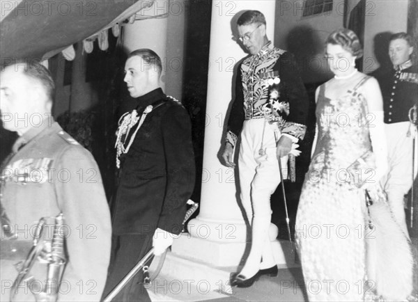 At an investiture at Government House. Sir Maurice Hallett, governor of the United Provinces, and Lady Hallett preceded by George Boon ADC at an investiture at Government House. The men are attired in various dress uniforms complete with medals and swords, while the woman is wearing a long sleeveless dress made from a shimery material. Allahabad, India, 16 January 1940. Delhi, Delhi, India, Southern Asia, Asia.