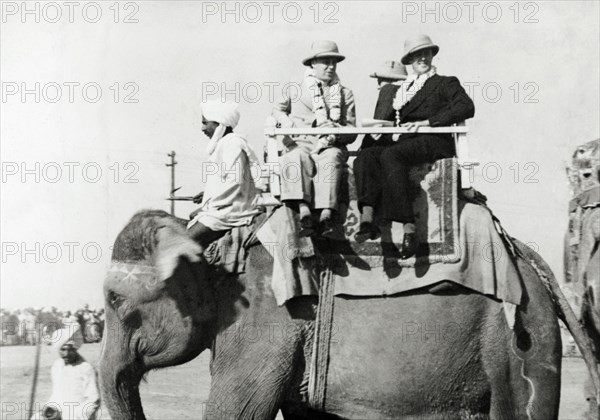 A ride on an elephant. George Boon: His Excellency Victor Hope, 2nd Marquess of Linlithgow and Viceroy of India are sitting in a howdah atop an elephant. There is also a mahout sitting across the elephant's neck. The westerners are wearing solartopis, leis and overcoats.United Provinces (Uppar Pradesh), India, 1940. Delhi, Delhi, India, Southern Asia, Asia.